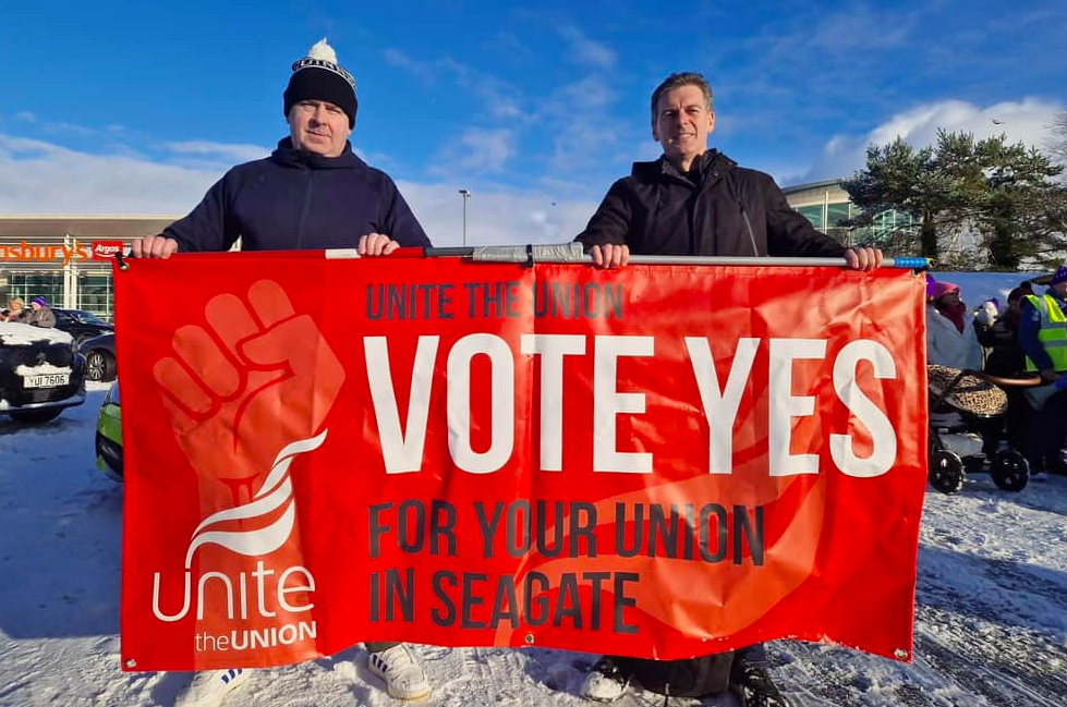 People Before Profit's Councillor Shaun Harkin holding Unite's Seagate Vote Yes for your Union banner in the snow with workers